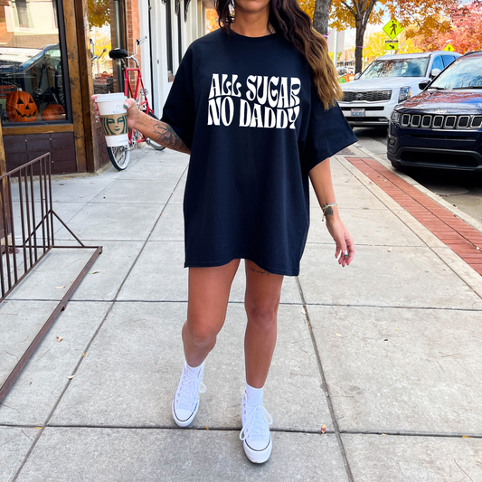 A woman holding a coffee and wearing a black oversized tshirt that says all sugar no daddy in white text
